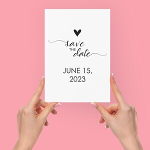 May include: A white card with black text that reads "Save the date" with a small black heart above the text. The date June 15, 2023 is printed below the text.