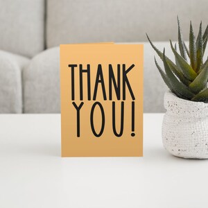 May include: A thank you card with the words "THANK YOU!" in black lettering on a light orange background.