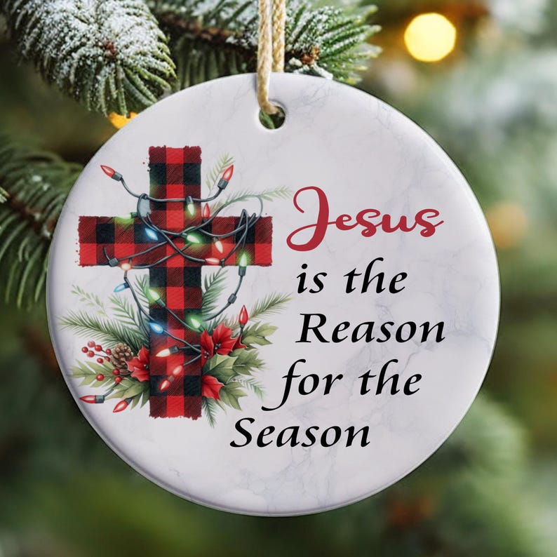 May include: A white ceramic Christmas bauble featuring a red and black checked cross adorned with Christmas lights and the text "Jesus is the Reason for the Season".