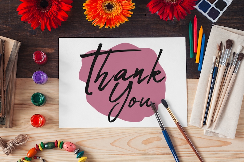 May include: A white card with the words "Thank You" written in black script on a pink watercolour background. The card is surrounded by paintbrushes, paint, and flowers.