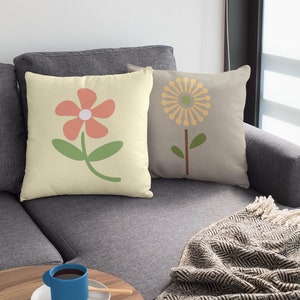May include: Two throw pillows with floral designs. The pillow on the left has a light yellow background with a pink flower and green stem. The pillow on the right has a light grey background with a yellow flower and green stem.