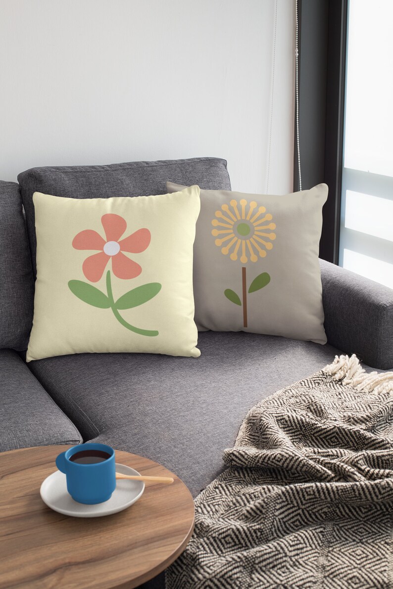 May include: Two throw pillows with floral designs. The pillow on the left has a light yellow background with a pink flower and green stem. The pillow on the right has a light grey background with a yellow flower and green stem.