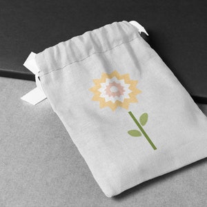 May include: A white drawstring bag featuring a yellow, pink and white flower design. The bag is made from a soft, natural fabric.