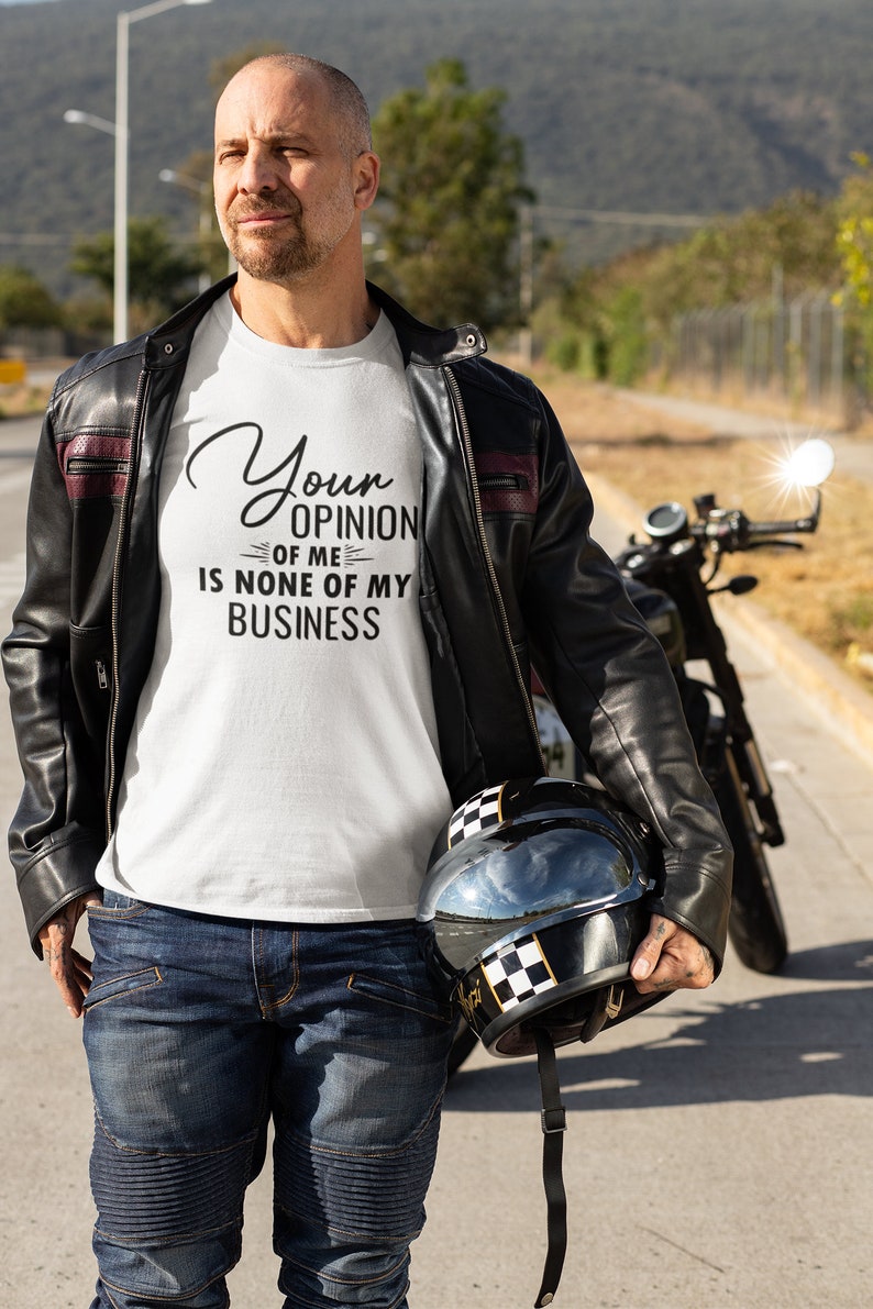May include: A white t-shirt with the text "Your opinion of me is none of my business" printed on it. The person is wearing a black leather jacket and blue jeans.