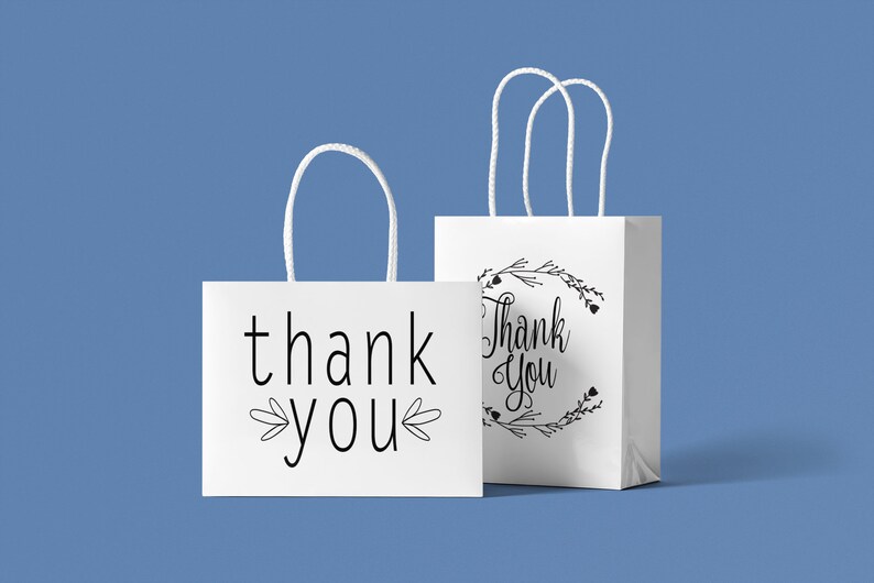 May include: Two white paper gift bags with black handles. One bag says "thank you" with a simple floral design. The other bag says "Thank You" with a more elaborate floral design.