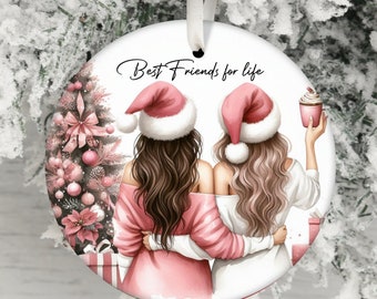 Puede incluir: Adorno navideño redondo con dos mujeres con gorros de Papá Noel, abrazándose, frente a un árbol de Navidad. El adorno tiene el texto "Best Friends for life" y está decorado con elementos rosas y blancos.