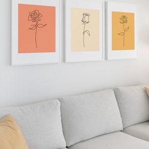 May include: Three framed line drawings of roses in different colors. The first rose is on a peach background, the second is on a cream background, and the third is on a yellow background.