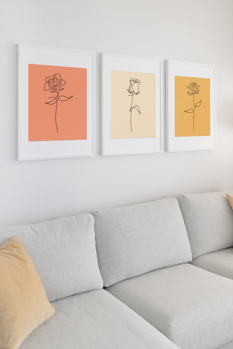 May include: Three framed line drawings of roses in different colors. The first rose is on a peach background, the second is on a cream background, and the third is on a yellow background.