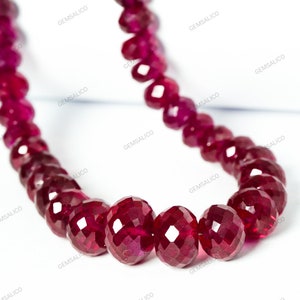 May include: A strand of deep red ruby beads, faceted and round, strung together to form a necklace. The beads are polished and have a glossy finish.