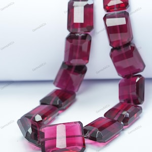 May include: A necklace or bracelet composed of deep red, rectangular-cut gemstones. The gems are faceted and strung together. The background is white, and the text "GemsAliCo" is repeated throughout the image.