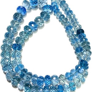 Könnte beinhalten: Eine Kette aus facettierten Aquamarin-Perlen in einem Farbverlauf von Blautönen. Die Perlen sind rund und haben eine facettierte Oberfläche. Die Perlen sind auf einem durchsichtigen Faden aufgefädelt.