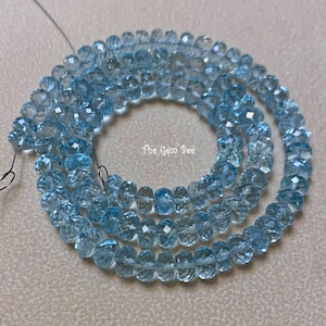May include: A strand of light blue aquamarine beads. The beads are faceted and have a slightly rounded shape. The beads are strung on a wire and are approximately 6mm in diameter. The Gem Bee is printed on a white label.