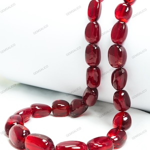May include: A necklace featuring large, oval-shaped, translucent red beads. The beads are strung together, creating a continuous loop. The necklace is displayed against a white background.
