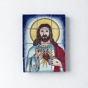 May include: A religious artwork depicting Jesus Christ, rendered in a folk art style. The image features a halo, a heart, and a blue, red, and white color palette. The artwork is composed of multiple tiles.