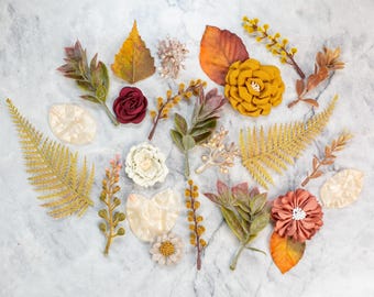 May include: Assortment of autumn-themed craft supplies, including faux leaves, flowers, and ferns in shades of red, orange, yellow, and green.