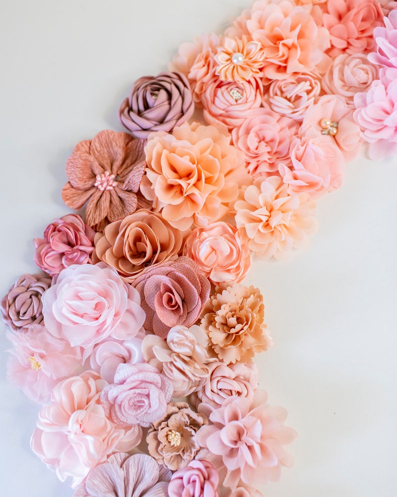 Puede incluir: Una colecci&oacute;n de flores de tela en tonos rosa y melocot&oacute;n. Las flores est&aacute;n dispuestas en un patr&oacute;n de degradado, con los tonos m&aacute;s oscuros en la parte inferior y los tonos m&aacute;s claros en la parte superior.