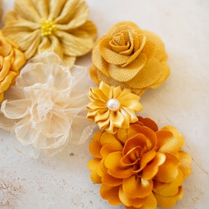K&ouml;nnte beinhalten: Sortiment gelber Stoffblumen mit Perlenakzent. Die Blumen sind aus verschiedenen Materialien gefertigt, darunter Seide, Satin und Chiffon.