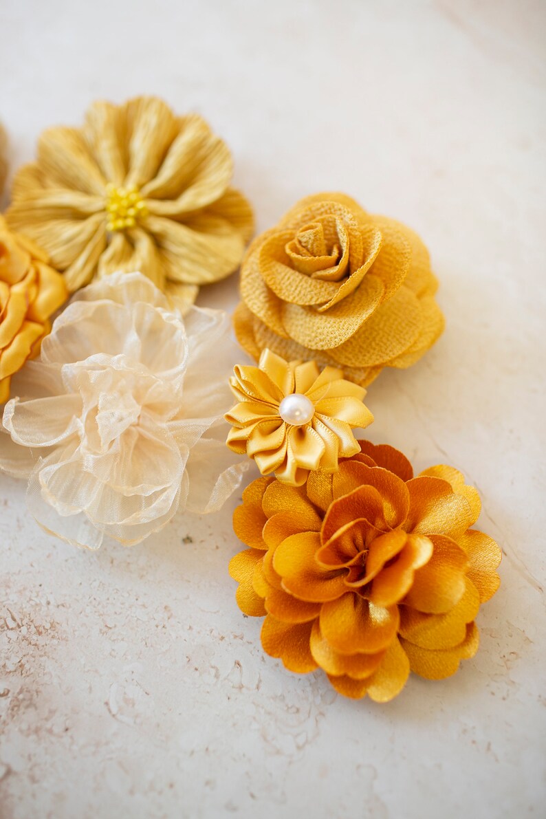 K&ouml;nnte beinhalten: Sortiment gelber Stoffblumen mit Perlenakzent. Die Blumen sind aus verschiedenen Materialien gefertigt, darunter Seide, Satin und Chiffon.