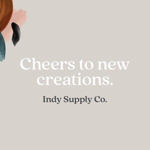 Puede incluir: Un fondo gris claro con formas abstractas de acuarela en tonos marrones, rosas y verde azulado. El texto "Cheers to new creations." est&aacute; escrito en blanco, seguido de "Indy Supply Co." en negro.