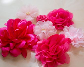 May include: An assortment of fabric flowers in shades of pink and fuchsia. The flowers vary in size and style, with some featuring multiple layers of petals. The arrangement includes a small rose and several larger blooms.