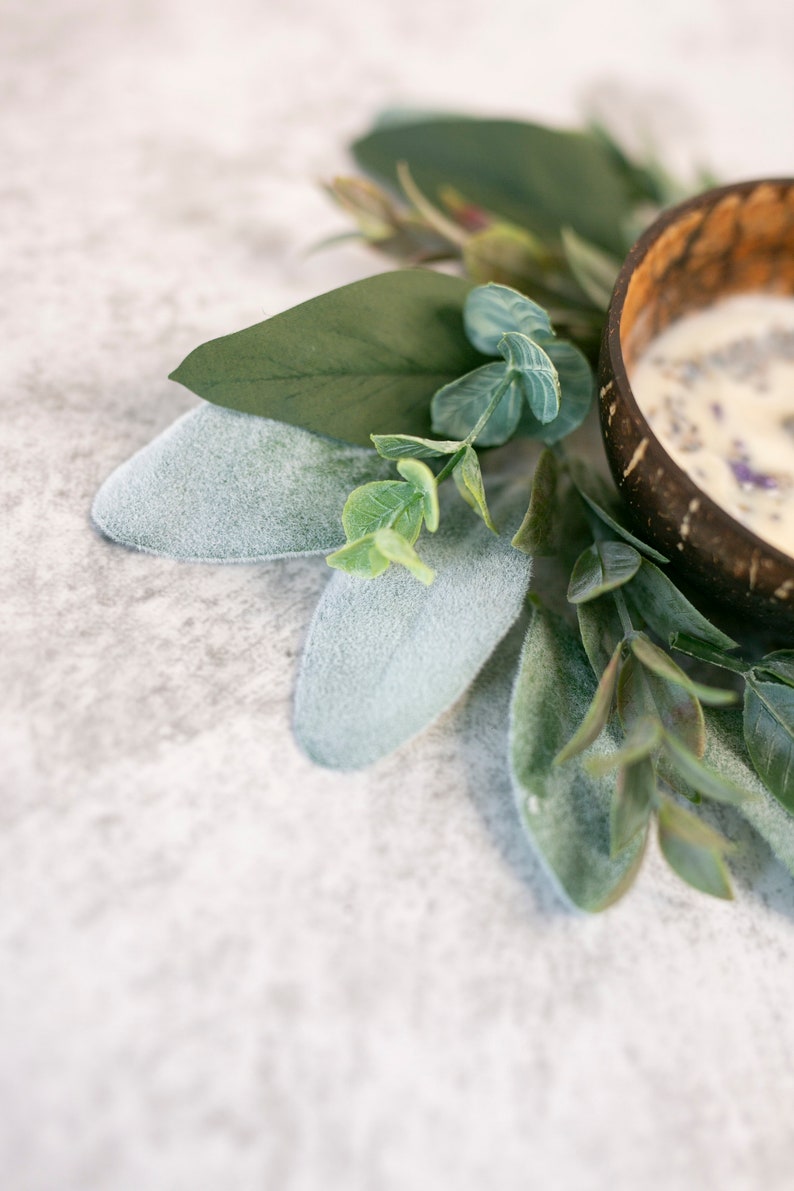 Puede incluir: Un peque&ntilde;o cuenco blanco hecho de c&aacute;scara de coco, lleno de una sustancia blanca y flores de lavanda secas. El cuenco est&aacute; rodeado de hojas verdes.