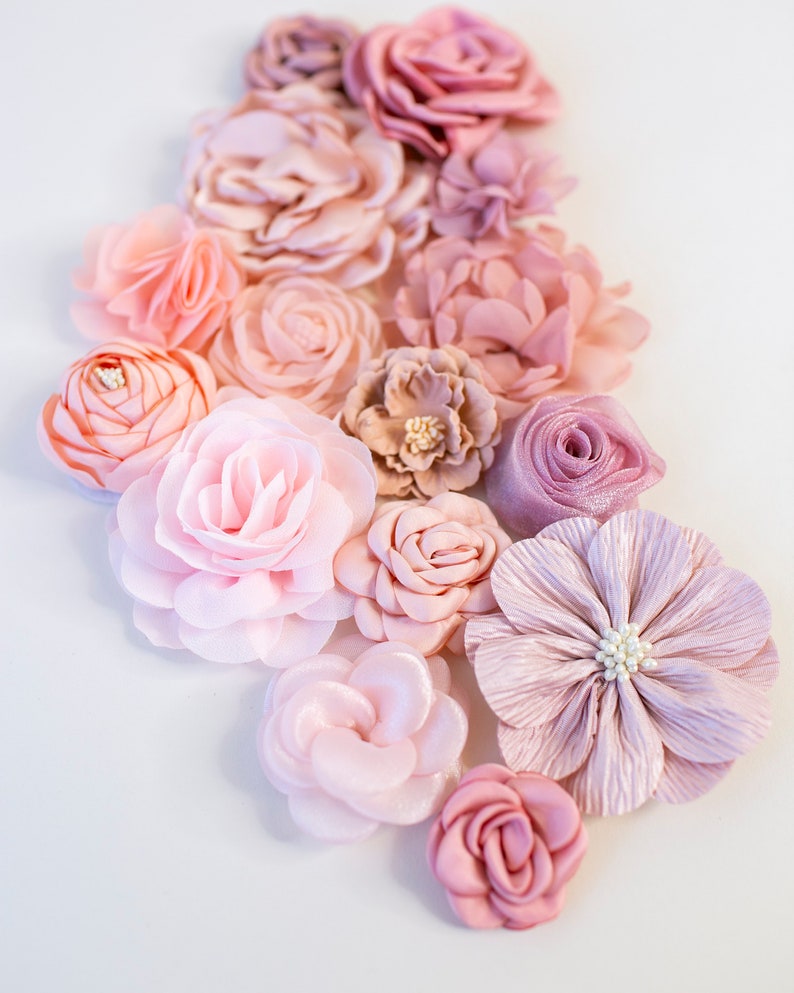 Puede incluir: Una colecci&oacute;n de flores de tela rosa y rubor, dispuestas en un patr&oacute;n en cascada. Las flores est&aacute;n hechas de varios materiales, incluyendo seda y sat&eacute;n, y tienen un aspecto delicado y femenino.