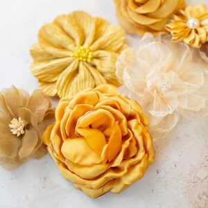 K&ouml;nnte beinhalten: Sortiment gelber Stoffblumen, darunter eine Rose, eine G&auml;nsebl&uuml;mchen und eine gekr&auml;uselte Blume. Die Blumen sind auf einem wei&szlig;en Hintergrund angeordnet.