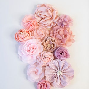 Puede incluir: Una colecci&oacute;n de flores de tela rosa y rubor en varios tama&ntilde;os y formas. Las flores est&aacute;n dispuestas en un grupo sobre un fondo blanco.