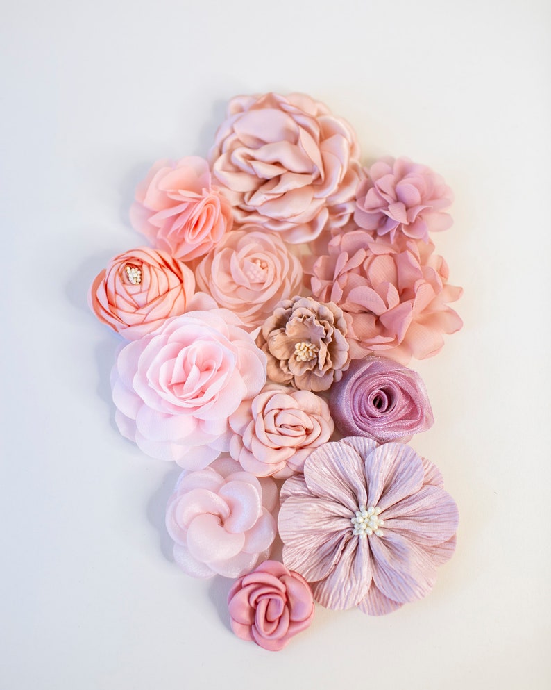 Puede incluir: Una colecci&oacute;n de flores de tela rosa y rubor en varios tama&ntilde;os y formas. Las flores est&aacute;n dispuestas en un grupo sobre un fondo blanco.
