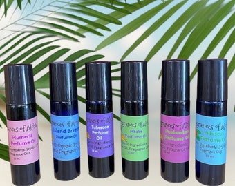 May include: Six small, black roll-on bottles of perfume oil with colorful labels. The labels feature the text "Fragrances of Aloha" and the names of different scents: Plumeria, Island Breeze, Tuberose, Pikake, Puakenikeni, and Hibiscus. Each bottle contains 10 ml of perfume oil.
