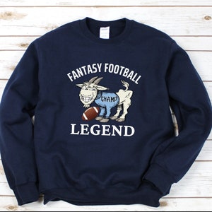 May include: A navy blue sweatshirt with a white graphic of a goat holding a football. The goat is wearing blue pants with the word "Champ" on them. The text "Fantasy Football Legend" is printed above the goat.