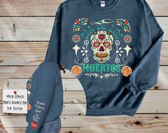 May include: A dark blue sweatshirt with a colorful Day of the Dead sugar skull design. The text "Dia de los Muertos" is printed below the skull. The sweatshirt has a long sleeve and a crew neck.