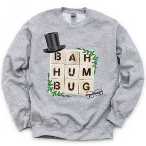 May include: A gray sweatshirt with a Christmas-themed design featuring a top hat, glasses, and wooden blocks spelling out "Bah Hum Bug".