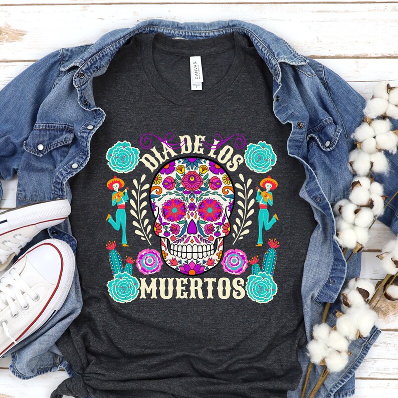 May include: A dark grey t-shirt with a colorful sugar skull design and the text "Dia de los Muertos" in purple lettering.