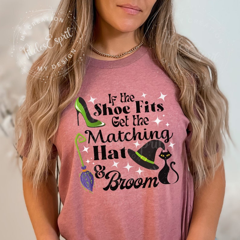 May include: Mauve t-shirt with the text "If the Shoe Fits Get the Matching Hat & Broom." The design includes a green high heel, a witch's hat, a black cat, and a broom. The shirt is decorated with white stars.