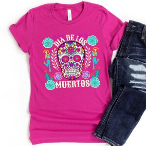 May include: A pink t-shirt with a colorful sugar skull design and the text "Dia de los Muertos".