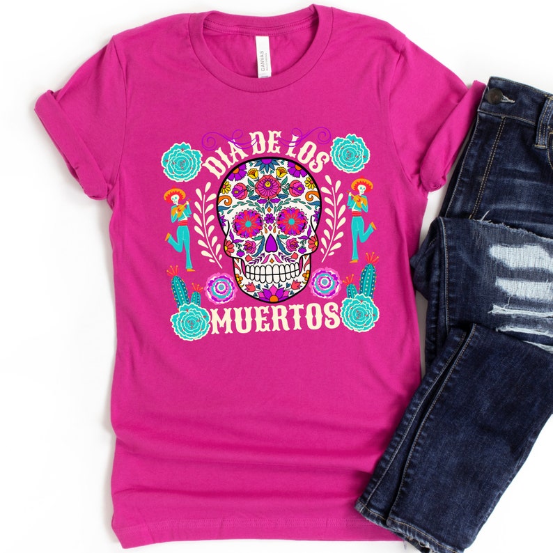 May include: A pink t-shirt with a colorful sugar skull design and the text "Dia de los Muertos".