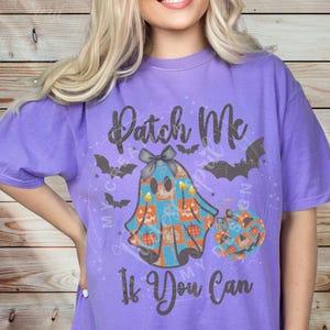 May include: A purple t-shirt with the text "Patch Me If You Can". The shirt features a graphic of a ghost with a bow, pumpkins, and bats, perfect for Halloween.