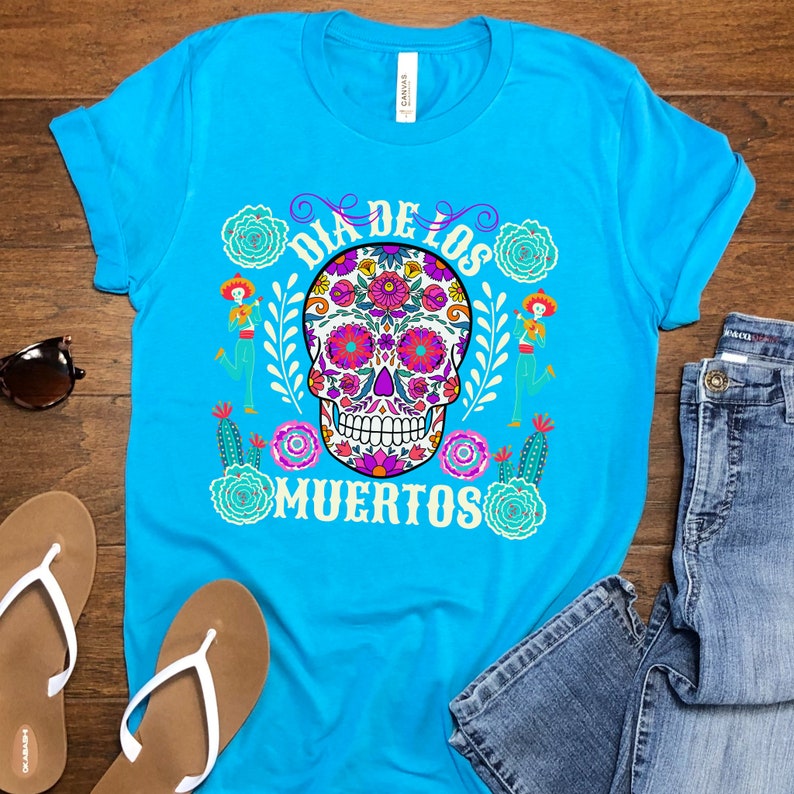 May include: A turquoise blue t-shirt with a colorful sugar skull design and the text "Dia de los Muertos".