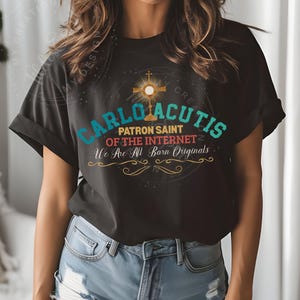 May include: Black t-shirt with a graphic design featuring the words "Carlo Acutis Patron Saint of the Internet We Are All Born Originals" in colorful text. The graphic also includes a gold cross and a halo.