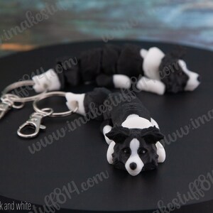 May include: Two black and white border collie dog keychains with silver key rings. The keychains are made of polymer clay and are attached to a black surface.