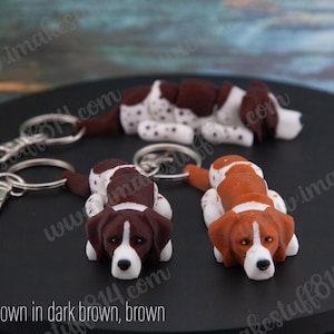 May include: Two dog keychains, one brown and white, one brown and white with orange accents. Both are lying on a black surface.