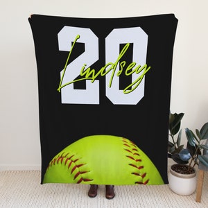 May include: Black and white softball jersey with the number 20 and the name "Lindsey" in green script. A yellow softball is at the bottom of the jersey.