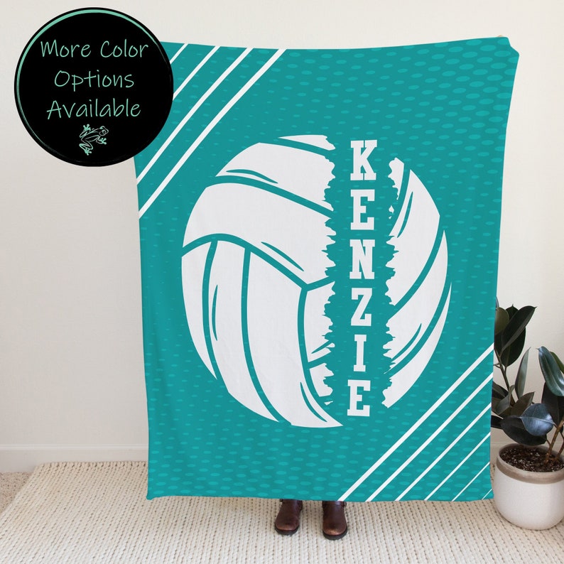 Puede incluir: Manta de voleibol turquesa y blanca con el nombre "KENZIE" escrito verticalmente a un lado del bal&oacute;n de voleibol.
