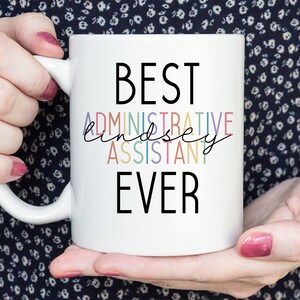 May include: White ceramic mug with black text that reads "BEST ADMINISTRATIVE ASSISTANT EVER". The word "ADMINISTRATIVE ASSISTANT" is in rainbow colors.