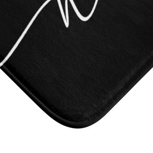 May include: Black bath mat with a white cursive "Home" design.