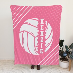Puede incluir: Manta de voleibol rosa y blanca con el nombre "KENZIE" escrito verticalmente a un lado del bal&oacute;n de voleibol.