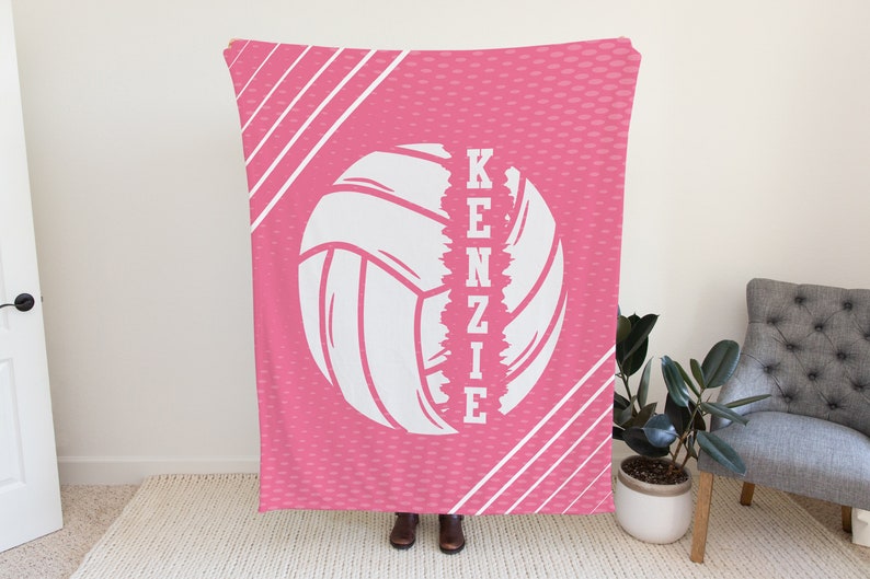 Puede incluir: Manta de voleibol rosa y blanca con el nombre "KENZIE" escrito verticalmente a un lado del bal&oacute;n de voleibol.
