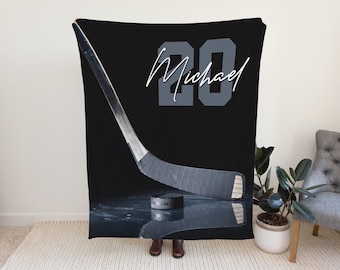 May include: Black blanket with a hockey stick and puck design. The number "20" and the name "Michael" are in white and grey. The blanket has a reflective surface, creating an ice rink effect. A great gift for hockey fans.