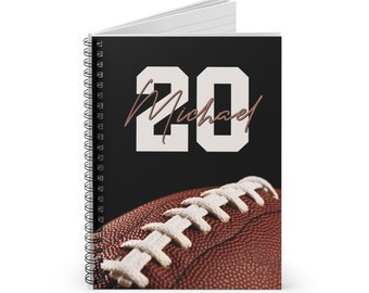 May include: A black spiral notebook with a white football number 20 and the name Michael in brown script. The bottom of the notebook features a close-up of a brown football with white laces.